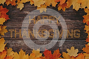 Happy Thanksgiving greeting text on wooden background with frame of maple leaves