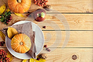 Happy Thanksgiving holiday background. Pumpkins, fallen leaves, plate, apples, red berries on wooden table. Thanksgiving dinner