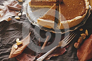 Happy Thanksgiving. Pumpkin pie on parchment paper on rustic table with linen napkin, autumn leaves, anise, cinnamon and cutlery.