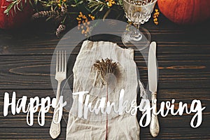 Happy thanksgiving text on plate, cutlery,  napkin on wooden table with pumpkins and autumn flowers, dinner rustic setting.