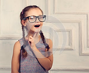 Happy thinking kid girl in fashion glasses with excited emotional face looking on studio background. Closeup toned portrait