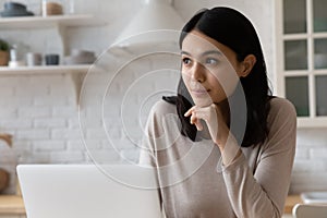 Happy thoughtful Asian student girl sitting at laptop