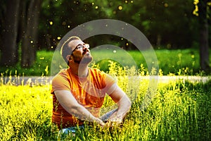 A happy thoughtful dreamer man is sitting on green grass in park