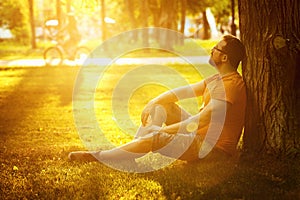 A happy thoughtful dreamer man is sitting on green grass in park photo