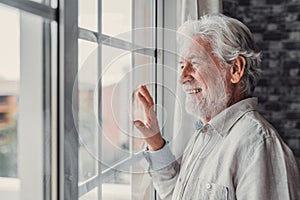 Happy thoughtful older 70s man looking out of window away with hope, thinking of good health, retirement, insurance benefits,