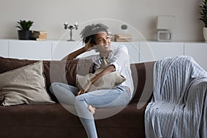 Happy thoughtful young black woman, African girl relaxing on couch