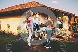 Happy three children are jumping on a trampoline in the garden near their house.