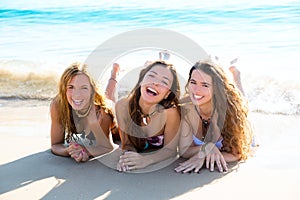 Happy three friends girls lying on beach sand smiling