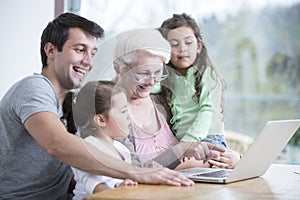 Happy three generation family using laptop at table in house