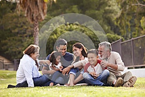 Happy three generation Hispanic family sitting on the grass together in the park, selective focus