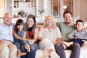 Happy three generation white family sitting on a sofa together at home smiling to camera, front view