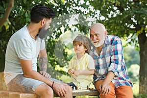 Happy three generations of men have fun and playing Chess in green park. Handsome grandpa and grandson are playing chess