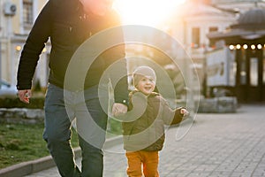 A happy three year old son walks hand in hand with his dad in the city on a sunny spring day