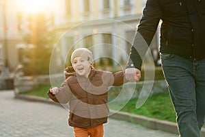 A happy three year old son walks hand in hand with his dad in the city on a sunny spring day. Family fun time and leisure.