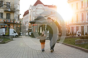 A happy three year old son walks hand in hand with his dad in the city on a sunny spring day. Family fun time and leisure.