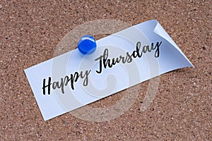 Happy Thursday text on white stick note and pinned to a cork notice board.