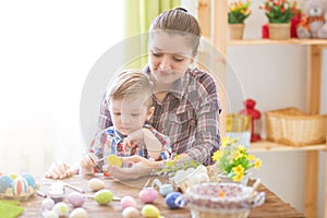 Happy time while painting easter eggs. Easter concept. Happy mother and her cute child getting ready for Easter by painting the eg