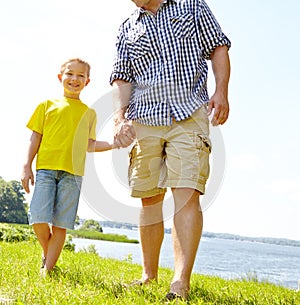 So happy to be spending time with dad. Cute son walking with his dad by the lake and holding his hand lovingly.