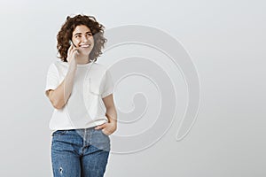 Happy to chit-chat with close friend. Studio portrait of happy carefree curly-haired woman in jeans and t-shirt