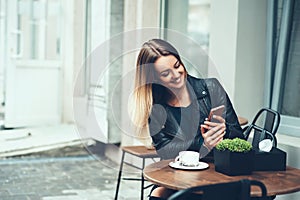 Always happy to communicate with friends. Beautiful young woman sitting in cafe typing message to her friend while drinking taste