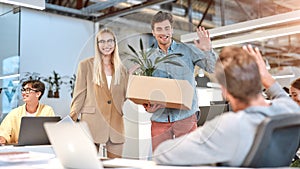 Happy to to see you in our team. Young handsome man in casual wear holding box with things and waving to his new