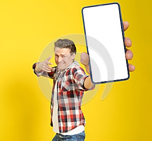 Happy to win handsome man pointing at smartphone with white empty screen, wearing red plaid shirt and jeans cellphone