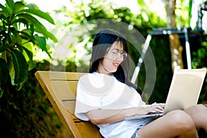 work Cheerful young Asian woman smiling while working on her laptop outside the office, at home, working in the park.