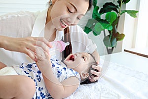 Happy toddle baby infant child lying on white bed while mother holding milk bottle for feeding her daughter kid girl, mom love and