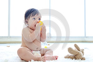 Happy toddle baby kid sitting on fluffy white rug floor in living room, little girl daughter playing with toys and put a toy in photo