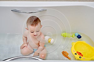 Happy toddler baby boy is playing with toys in the bathtub. A child play