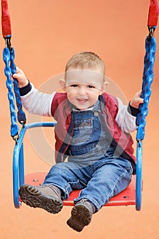 Happy toddler baby boy rides on a swing. Smiling child swinging on the