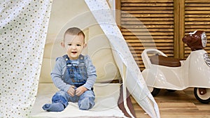 Happy toddler baby boy sitting in a children tent, playroom. Kid age one