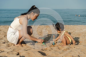 happy toddler baby girl playing sand toy with mother on the sea beach