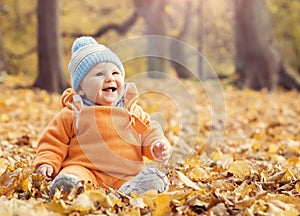 Happy toddler baby playing with leaves in autumn park.