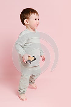 Happy toddler baby is playing with a toy car against a pink background