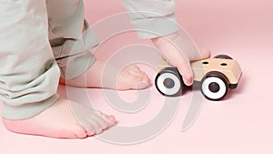 Happy toddler baby is playing with a toy car against a pink background