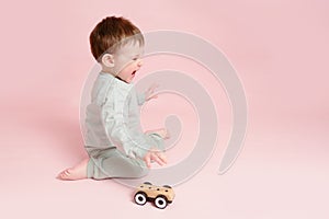 Happy toddler baby is playing with a toy car against a pink background