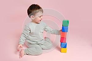 Happy toddler baby plays with cubes on studio pink background. Child