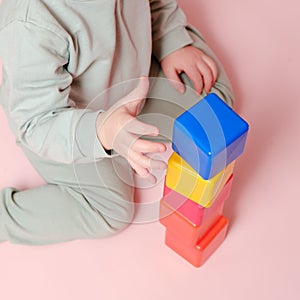 Happy toddler baby plays with cubes on studio pink background. Child