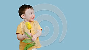 Happy toddler baby with tulip flower on studio blue background, copy s