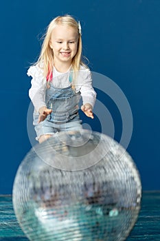 Happy toddler blonde girl havig fun while rolling giant disco ball on the floor
