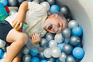 Happy toddler boy playing in a ball pit full of colorful balls. Sensory play at the nursery school for kids wellness