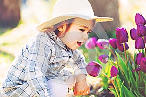 Happy toddler girl in a hat playing with purple tulips