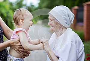 Happy toddler girl and her great grandmother holding hands and looking at one another