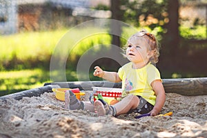 Happy toddler girl playing in sand on outdoor playground. Baby having fun on sunny warm summer sunny day. Active child