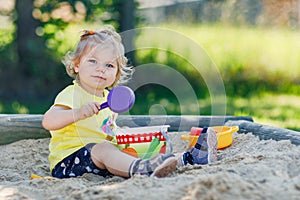 Happy toddler girl playing in sand on outdoor playground. Baby having fun on sunny warm summer sunny day. Active child