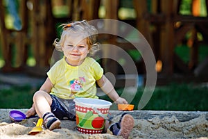 Happy toddler girl playing in sand on outdoor playground. Baby having fun on sunny warm summer sunny day. Active child