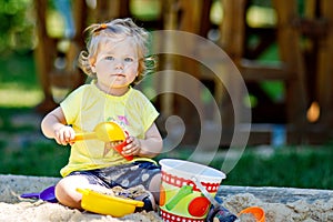 Happy toddler girl playing in sand on outdoor playground. Baby having fun on sunny warm summer sunny day. Active child