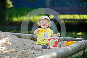 Happy toddler girl playing in sand on outdoor playground. Baby having fun on sunny warm summer sunny day. Active child