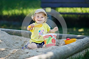 Happy toddler girl playing in sand on outdoor playground. Baby having fun on sunny warm summer sunny day. Active child